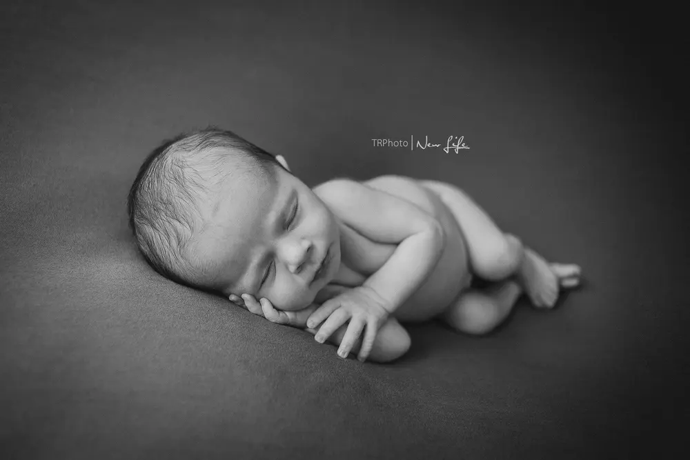 A newborn asleep on a dark blanket, black and white
